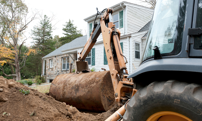 closeup of an excavator pulling a residential underground oil tank out of the ground